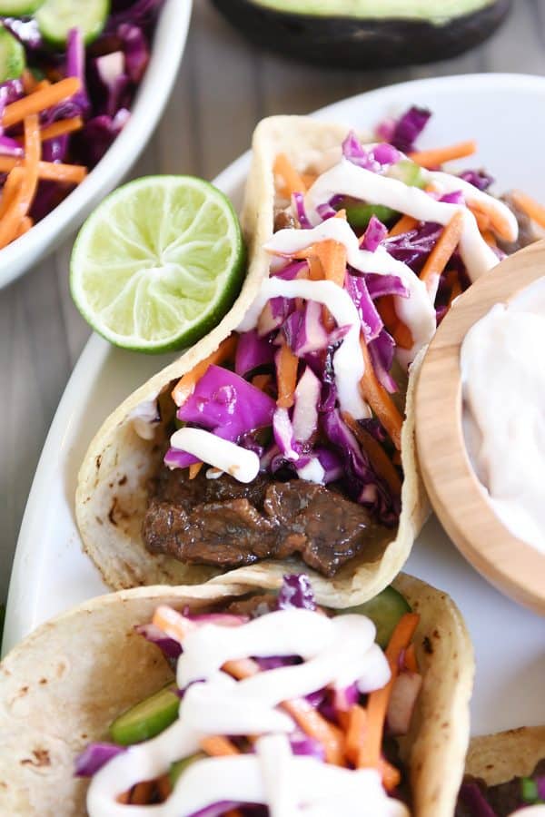 Top down view of Korean beef tacos with slaw and sauce on white platter.