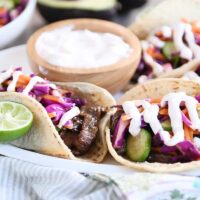Korean beef tacos with slaw and sauce on white platter.