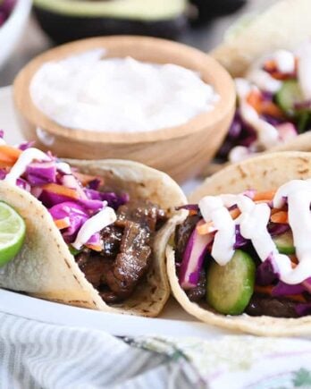 Korean beef tacos with slaw and sauce on white platter.