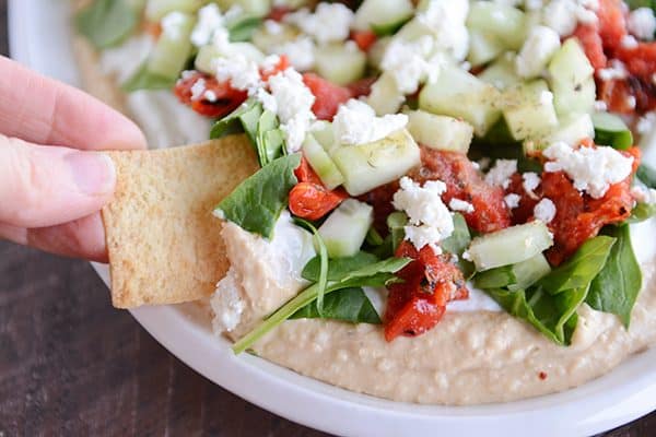 A cracker dipping into a bowl of greek hummus dip. 