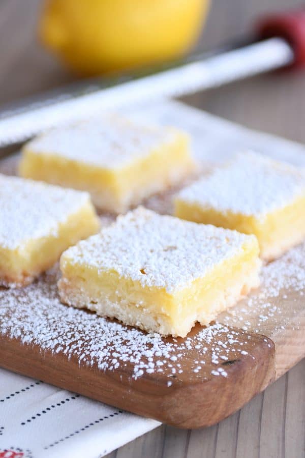 Lemon bars on cutting board sprinkled with powdered sugar.