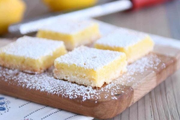 Lemon bars on cutting board sprinkled with powdered sugar.