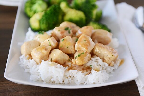 A white platter with cooked rice topped with lemon-glaze chicken and cooked broccoli on the side.