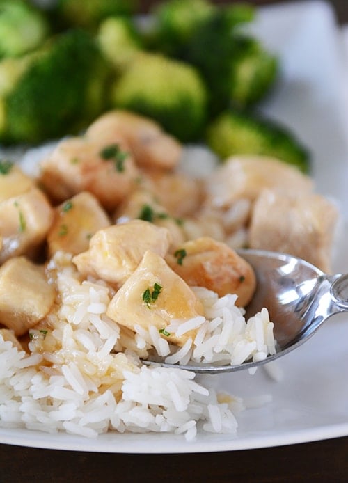 A spoon taking a bite of cooked white rice and lemon-glazed chicken. 