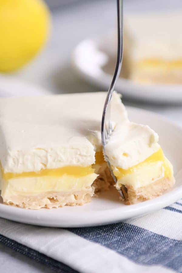 Lemon truffle shortbread bar on white plate with a fork taking a bite out. 