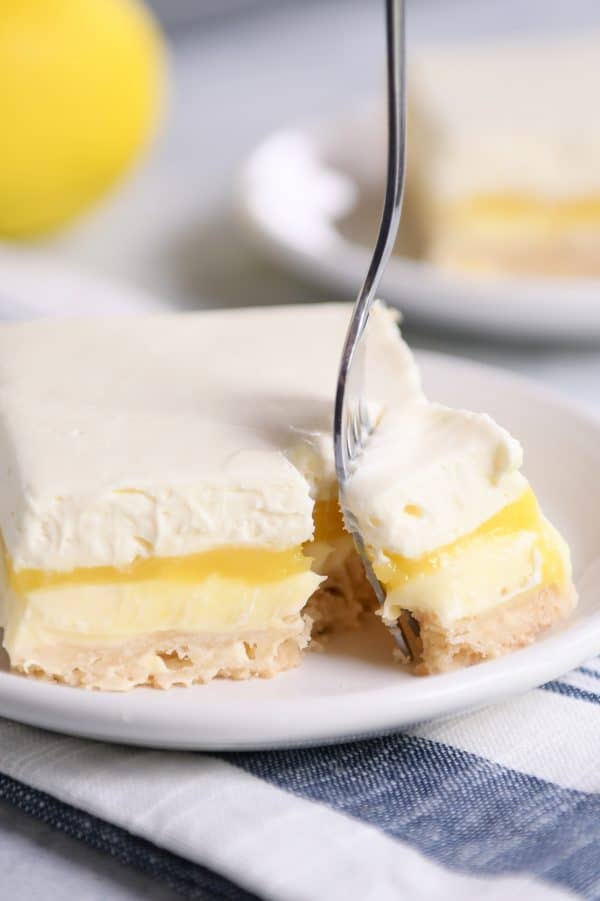 Lemon truffle shortbread bar on white plate with a fork taking a bite out.