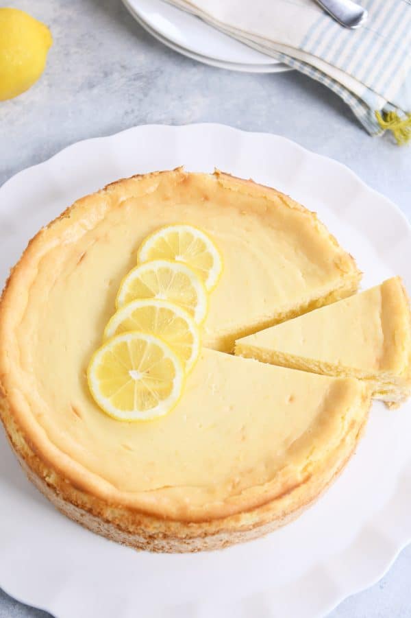 Lemon cheesecake with white chocolate on white platter and fresh lemons on top.