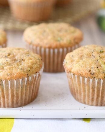 Several lemon poppy seed zucchini muffins on white plate.
