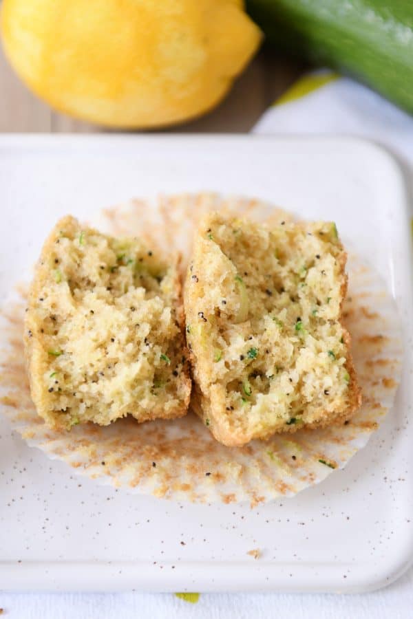 A lemon poppy seed zucchini muffin in half on a white plate.