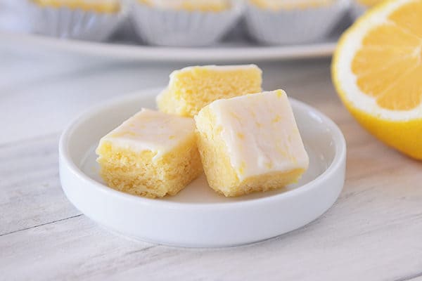 Three small iced lemon brownies on a white plate. 