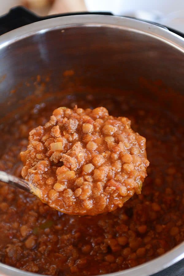 A metal ladle taking a scoop of beef and lentil chili out of a large pot. 