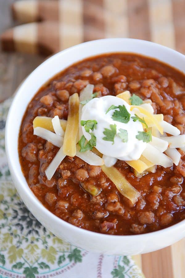 A white bowl full of sour cream and cheddar cheese-topped lentil beef chili.