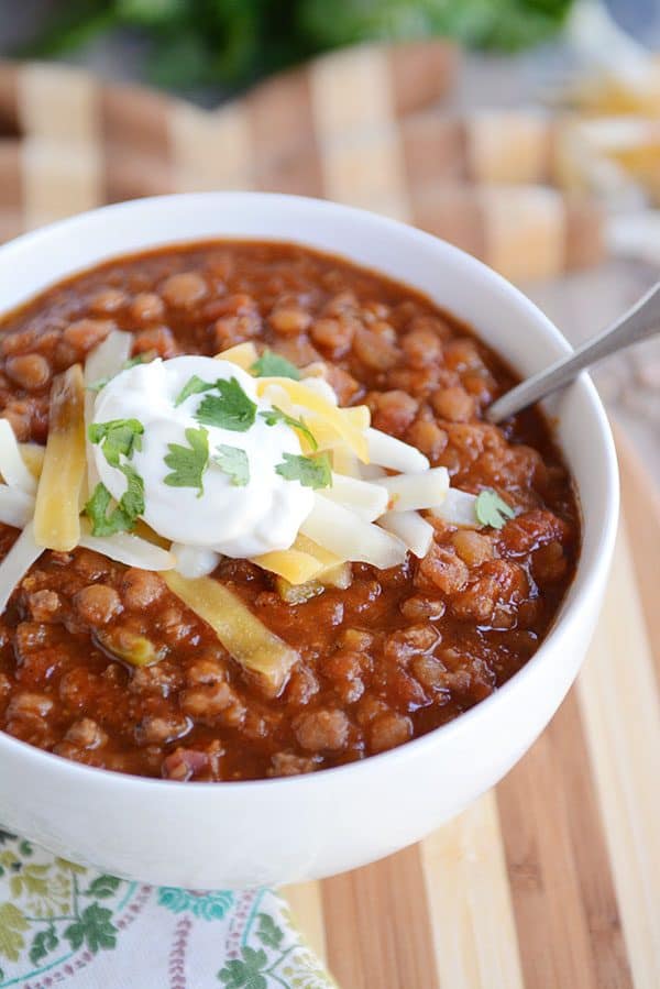 A white bowl of lentil chili topped with sour cream, cheddar cheese, and parsley.