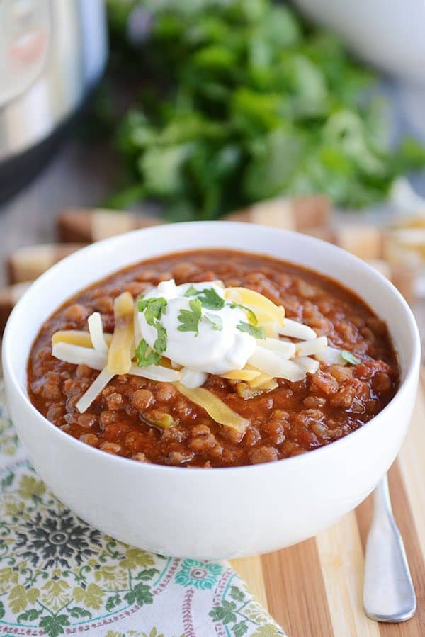 A white bowl full of lentil beef chili topped with sour cream and cheddar cheese.