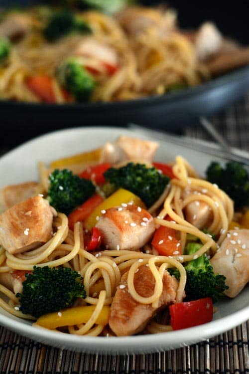 A plate and skillet full of chicken and vegetable lo mein. 