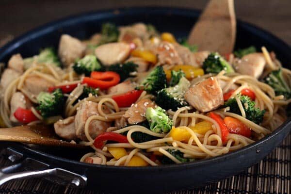 A cast iron skillet full of a lo mein, vegetable, and chicken stir fry. 