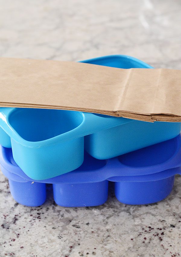 Two blue bento boxes with paper bags on top. 