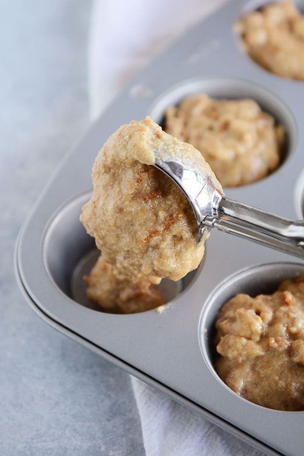 A muffin tin full of bran muffin batter, with an ice cream scoop filling the last slot in the muffin tin. 