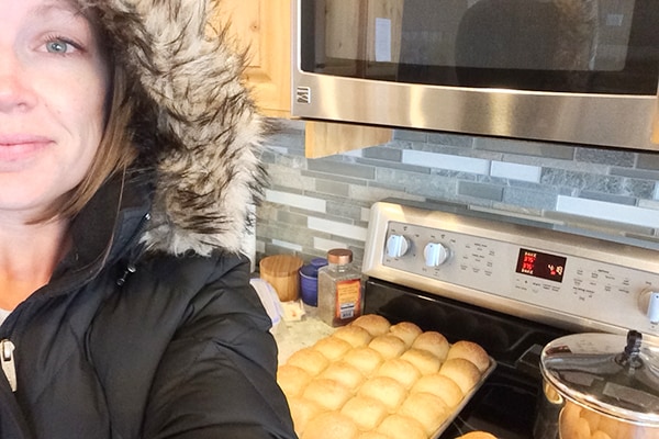 A woman cooking rolls in a winter parka. 