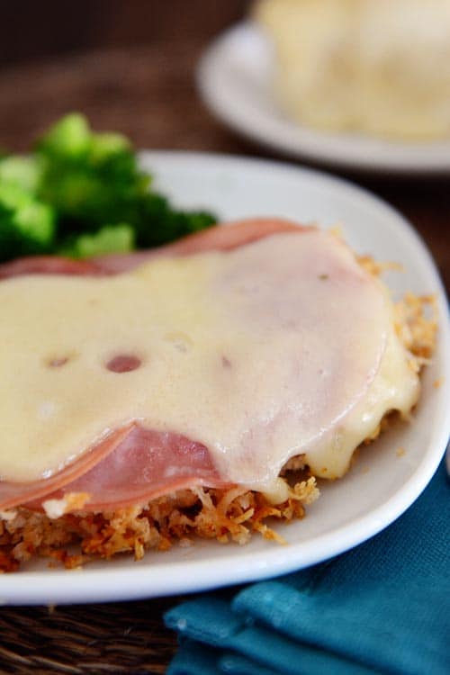 A swiss cheese and ham covered chicken breast on a white plate. 