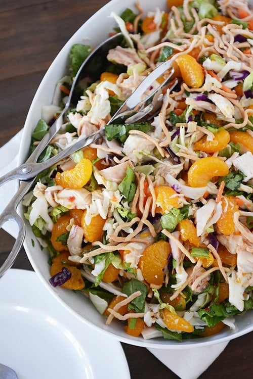 A white platter full of mandarin orange chicken salad with tongs on the side.