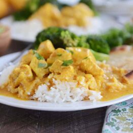 Thai chicken mango red curry sauce over white rice on white plate.