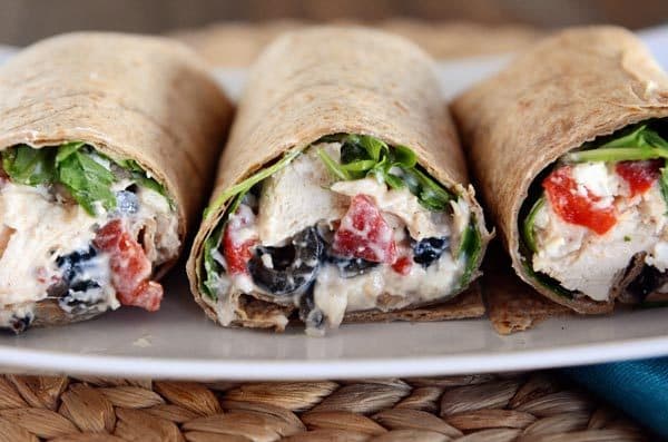 Side view of three mediterranean-filled chicken wraps on a white plate. 