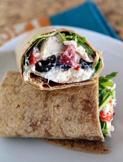 A mediterranean-filled chicken wrap cut in half on a white plate. 