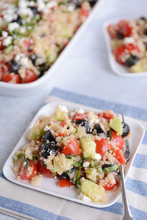 Top view of a square white plate with a large helping of Mediterranean quinoa salad.