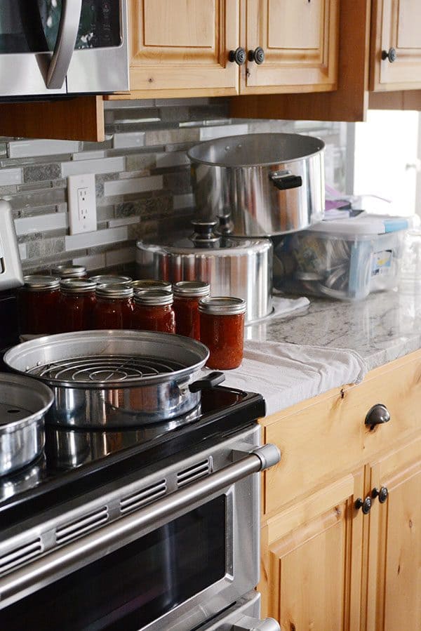 Canning supplies and canned salsa on a kitchen stove and countertop.