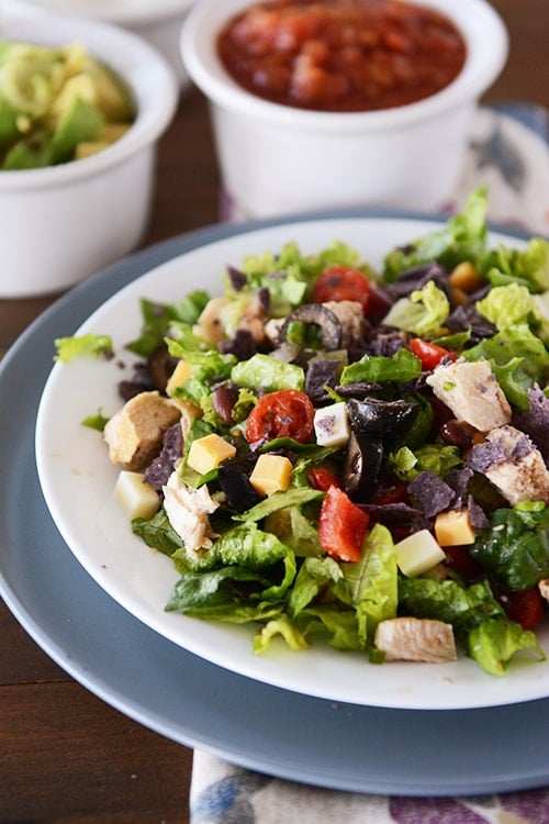 A white plate with Mexican chopped salad with chicken cubes, cheese cubes, olives and peppers.