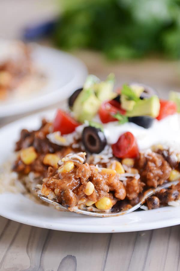 A fork taking a bite of Mexican haystack off a white plate of topping-covered haystack..