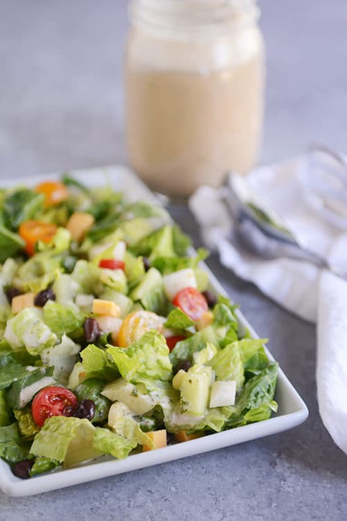 Chopped romaine salad with black beans, cubes of cheese, and cherry tomatoes sprinkled throughout, and a mason jar of dressing in the background.