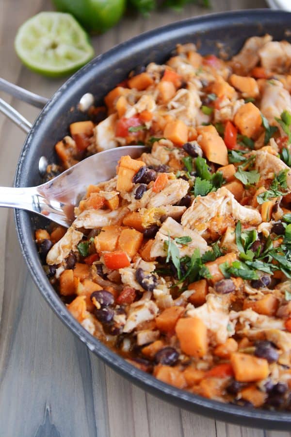 A spoon taking a scoop of cheesy sweet potato chicken mixture out of a skillet. 