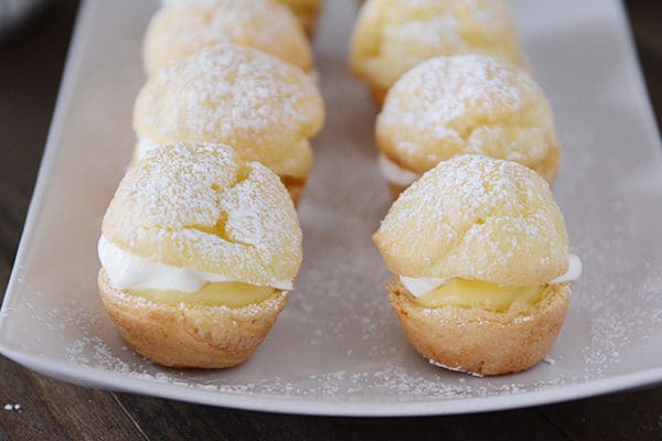 Powdered sugar dusted mini cream puffs on a white platter. 