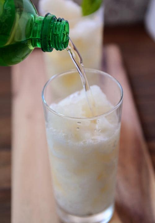Pop getting poured into a tall glass cup full of lemonade slush.