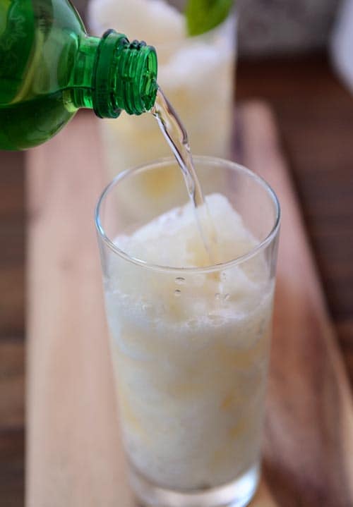 Pop getting poured into a tall glass cup full of lemonade slush. 