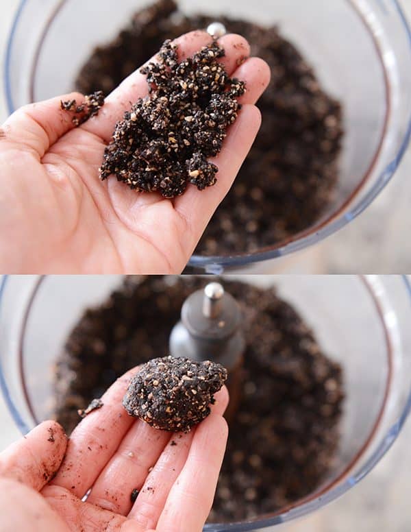 A hand holding dough of a dark chocolate almond joy bite ready to form it into a ball. 