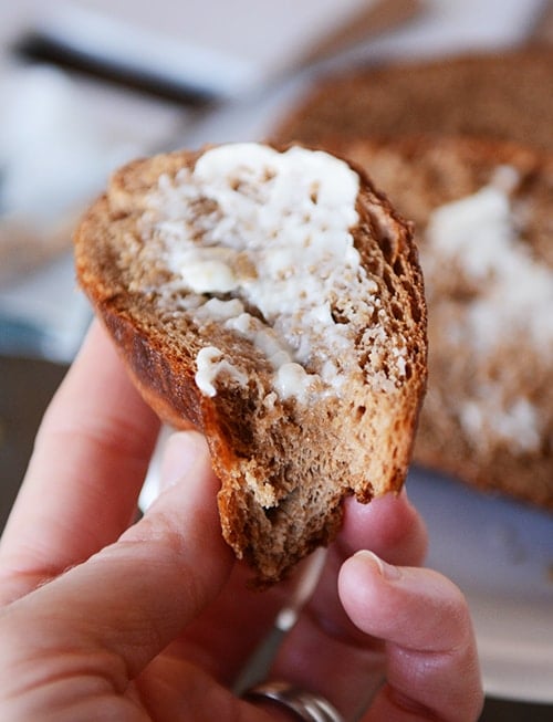 A hand holding a half-eaten piece of bread with butter on it. 