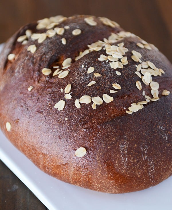 A dark colored loaf of bread with oats sprinkled on the top. 