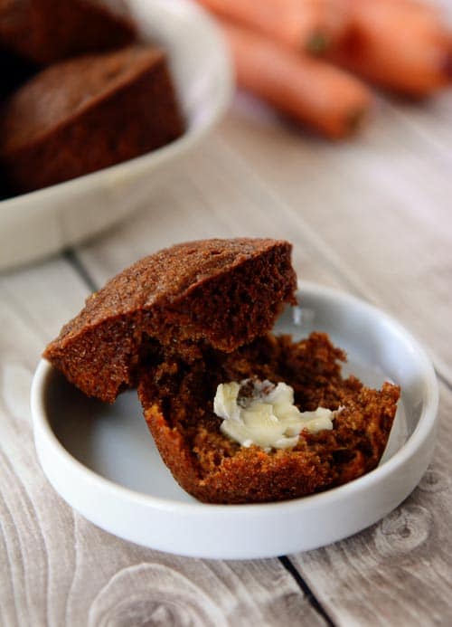 A golden brown muffin split in half with a pat of butter on the inside sitting in a small white ramekin.