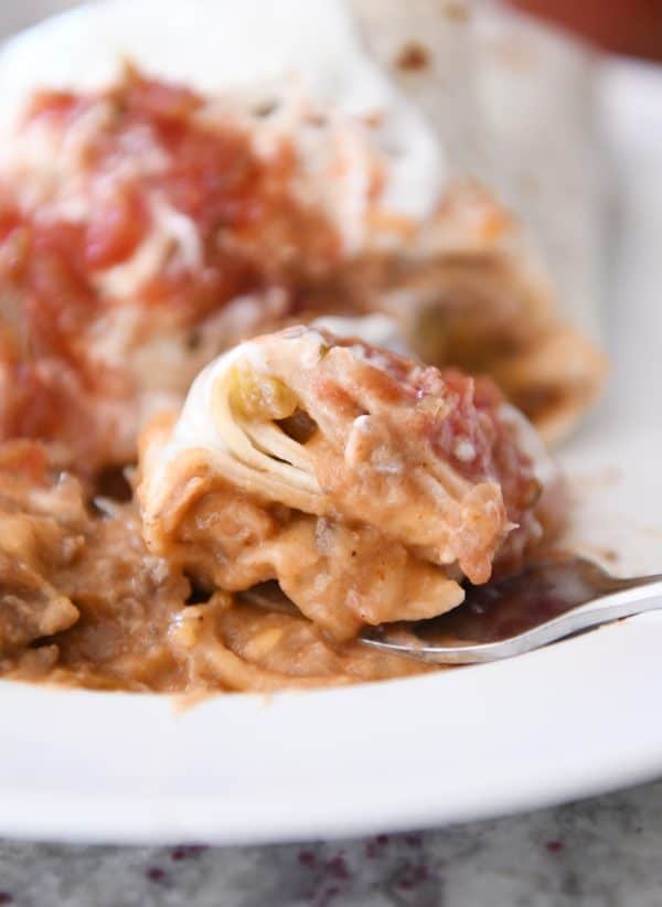 Cutting into the best freezer beef and bean burritos with bite on fork on white plate.