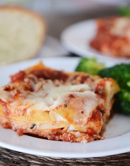 A piece of lasagna and broccoli on a white plate.