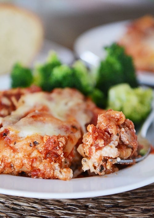 Broccoli and a piece of lasagna with a bite being taken out with a fork on a white plate.