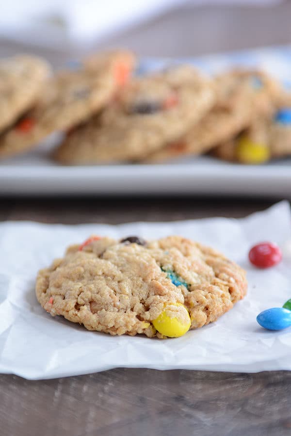 An M&M oat cookie on a piece of parchment with a tray of more cookies behind it.