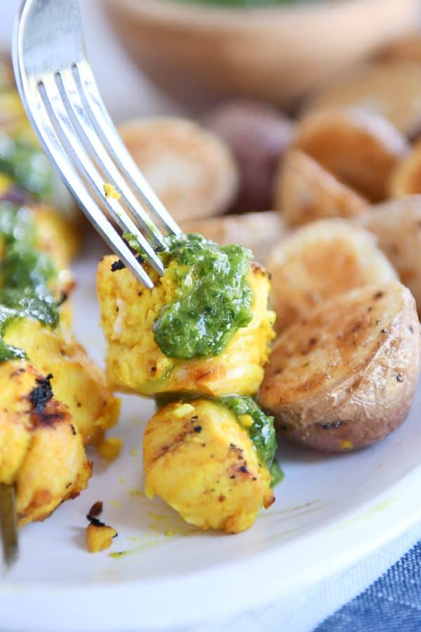 Fork poking a piece of Moroccan chicken skewer drizzled with green sauce. 