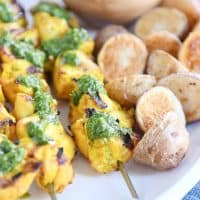 Close up view of green sauce on Moroccan chicken skewer with a couple roasted potatoes.