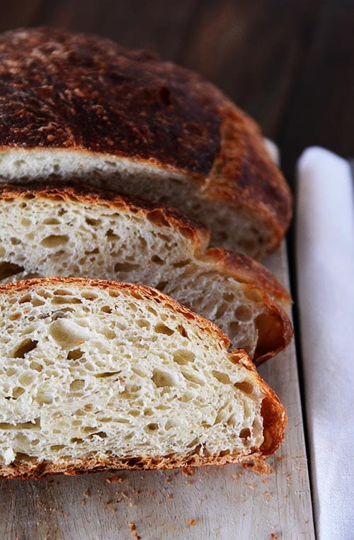 Top view of a baked loaf of artisan bread with two slices cut off of it.
