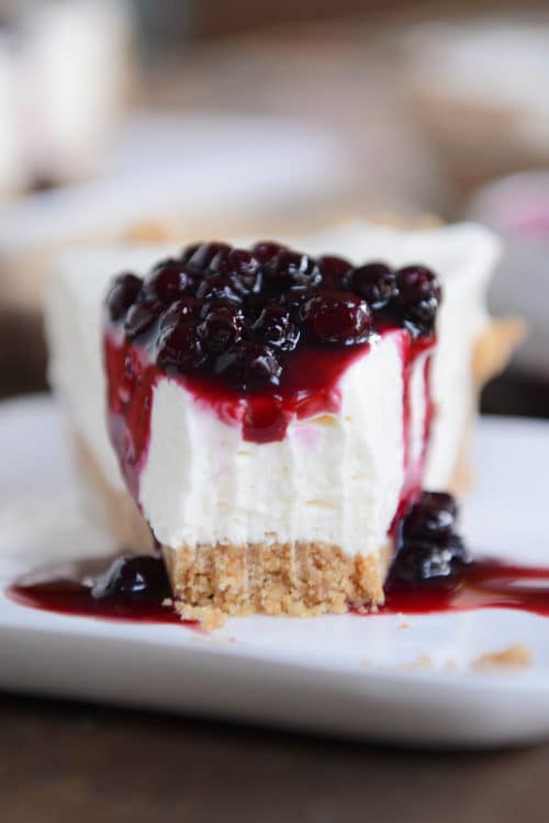 A slice of graham cracker crust no-bake cheesecake, with one bite taken out and blueberry sauce on top. 