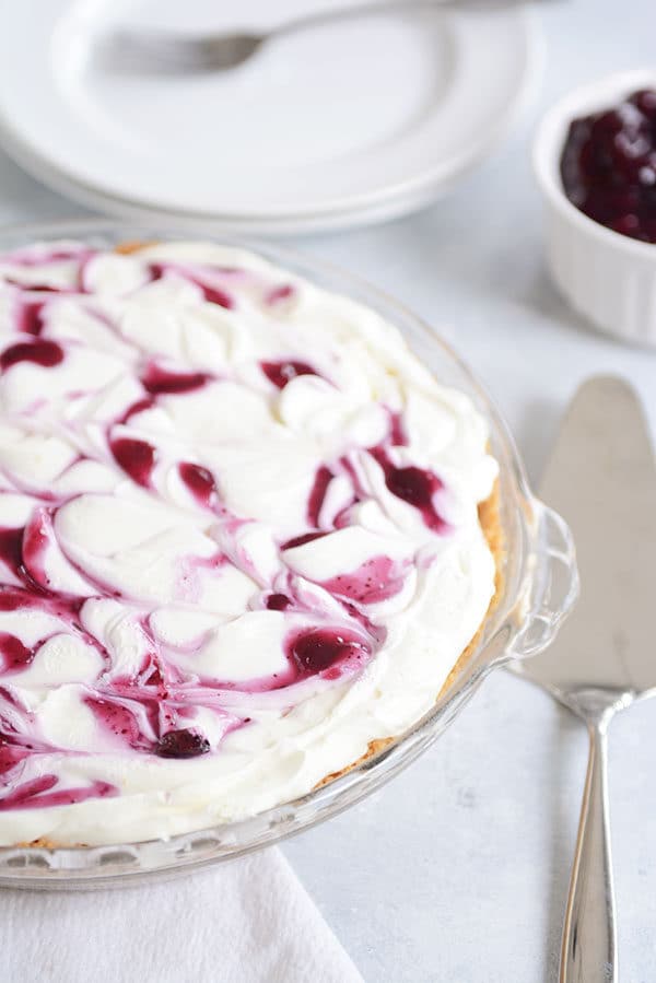 A blueberry swirled lemon cheesecake in a glass pie dish with a metal spatula beside it.